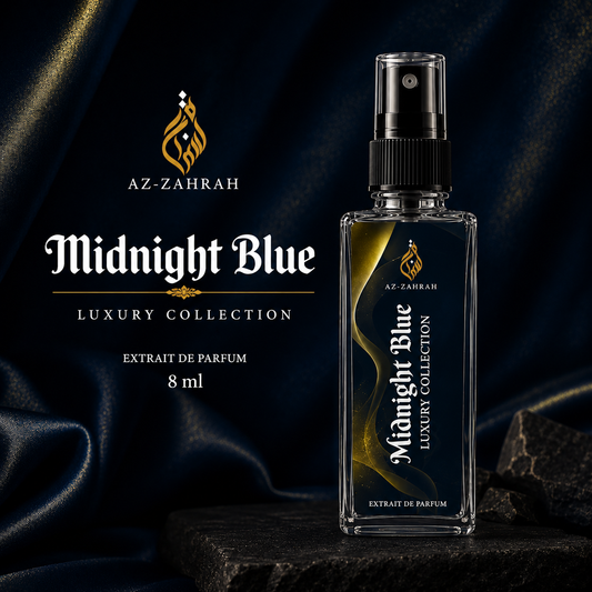 A clear rectangular perfume bottle labeled 'Midnight Blue Luxury Collection' by Az-Zahrah, standing on a dark stone surface against draped navy fabric. The bottle has a black spray top and a black-and-gold label.